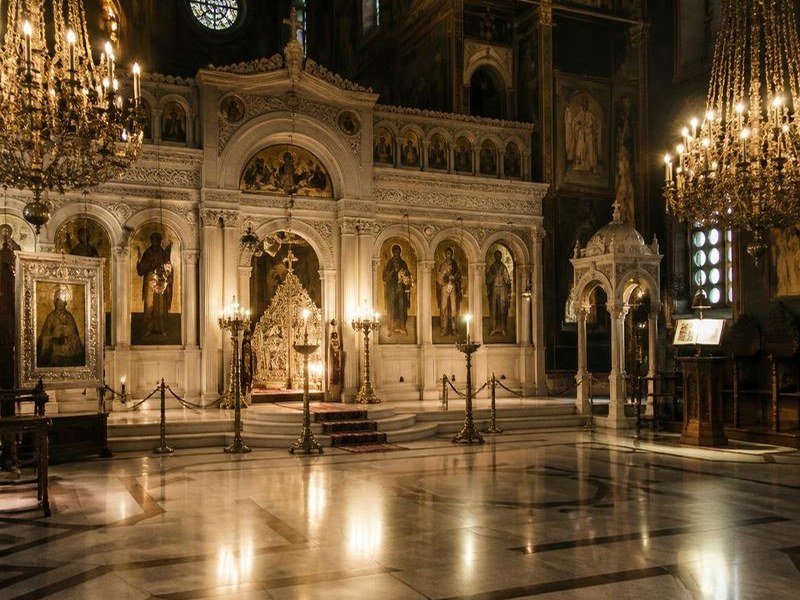 Candlelit interior of a Greek Orthodox church in Athens with gilded icons and frescoes