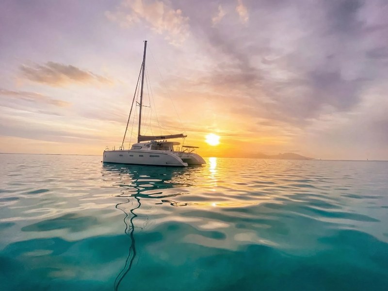 A white catamaran sailing on calm turquoise water off the Athens coast at golden hour