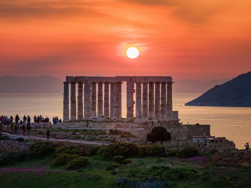 The Temple of Poseidon at Cape Sounio silhouetted against an orange sunset over the Aegean Sea